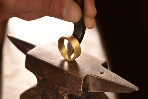 A gold ring being stamped with a hallmark.